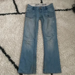 Blå bootcut jeans  - Snygga blå bootcut jeans från Diverse med broderad detalj på bakfickan och rosa sömmar. Innebenslängden 80 cm, midjemått rakt över 40 cm. Storlek W27. De är lite slitna längst ner på benet! Kom privat för fler frågor! Priset är förhandlingsbart. Läs bio innan köp! ❤️