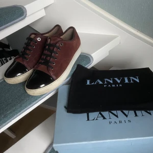 Lanvin skor  - Snygga vinröda skor från Lanvin i mocka med svarta lackdetaljer på tån och snörning. Skorna har en vit sula som ger en stilren kontrast. Perfekta för en trendig look. Storlek 41