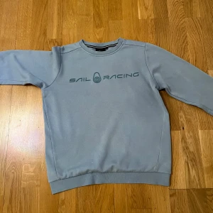 Blå tröja från Sail Racing - Säljer en stilren blå tröja från Sail Racing. Tröjan har en rund halsringning och långa. Sail Racing-logga på bröstet och ryggen. Perfekt för en ung grabb i storlek 150  