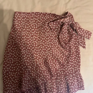 Rödblommig omlottkjol - Charmig röd omlottkjol med små vita blommor och volangdetaljer. Kjolen har en knytning i midjan som ger en fin passform. Perfekt för en somrig look! Från Shein 