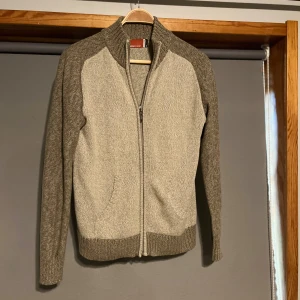 Stickad cardigan - Säljer en stilren kofta med dragkedja framtill. Koftan har en tvåfärgad design med mörkare grå ärmar och krage. Perfekt för kyliga dagar!