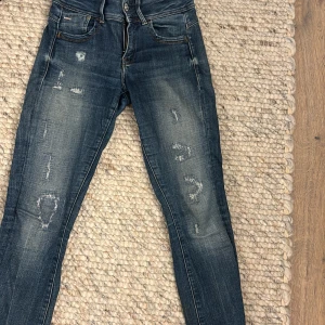 Blå jeans från G-Star RAW - Snygga blå jeans från G-Star RAW med en cool sliten look. De har en klassisk femficksdesign och är tillverkade i slitstarkt denim. Perfekta för en avslappnad stil.De är i skinny jeans. Storlek är 27 till 30 