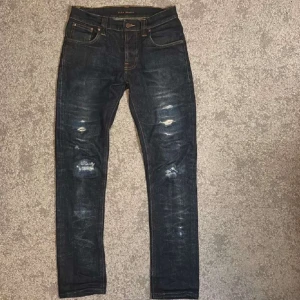 Mörkblå jeans med slitningar - Snygga mörkblå jeans från Nudie med coola slitningar på knäna. Sitter mer som 30:32. Bra skick! Hör av dig vid fler frågor!