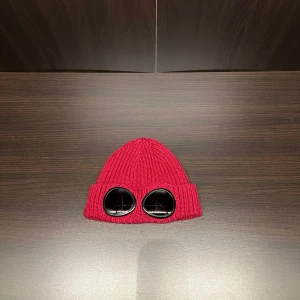 Röd ribbad C.P Company mössa - Snygg röd ribbad mössa med goggle framtill. Perfekt för att sticka ut i mängden och hålla sig varm under kyliga dagar.