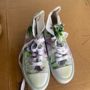 Blommiga sneakers från Attitude - Säljer ett par coola sneakers från Attitude med ett färgglatt blommönster. Skorna har snörning och en vit sula som ger en fräsch look. Perfekta för att liva upp vilken outfit som helst!