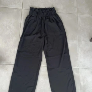 Svarta vida byxor - Snygga svarta byxor med hög midja och elastisk resår för extra komfort. Byxorna har en loose passform och är perfekta för en avslappnad stil. Tillverkade i ett mjukt material som ger en skön känsla hela dagen