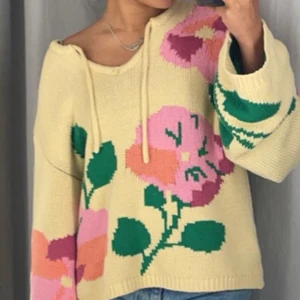 Gul stickad tröja med blommönster - Säljer en mysig gul stickad tröja med stora blommor i rosa och grönt. Tröjan har en avslappnad passform med långa ärmar och en knytning vid halsen. Perfekt för en färgglad och bekväm❤️👍