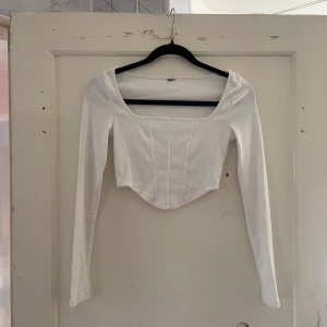 Vit långärmad croppad topp - Säljer en superfin vit långärmad topp som är croppad och har en snygg fyrkantig urringning. Perfekt för både vardag och fest! Den är i ett stretchigt material som sitter riktigt bra på kroppen.