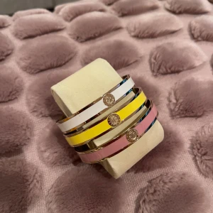 Armband från Dyrberg & Kern  - 2 guldfärgade armband i rostfritt stål från Dyrberg & Kern. Stelt med förslutning på baksidan och med  monogram. Nickelfri dansk design. Stl: 20 cm. Färgerna: Rosa och gul. 