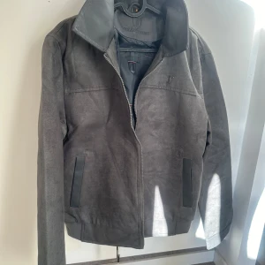 Italiensk Grå mockajacka  - Säljer en snygg grå mockajacka. Jackan har en stilren design med dragkedja framtill och två fickor. Den är perfekt för höst och vår, och ger en cool look med sin mjuka mockayta. Storlek M, passar perfekt för en normal passform.