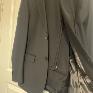 Svart kavaj från Dressmann - Säljer min Dressmann kostym då jag växt ur den. Den är sparsamt använd - endast på avslutningen av grundskolan och någon enstaka gång efteråt.   Storleken på kavajen är 46 Regular Slim fit och byxorna är 30/32 slim fit.   Går jättebra att komma och testa kostymen innan köp om så önskas. 