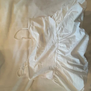 Vit topp från Divided - Säljer en söt vit topp från Divided med smala axelband och volangdetaljer. Perfekt för en somrig look. Toppen är i ett lätt och luftigt material. En liten fläck som går bort me lite kärlek i tvätten