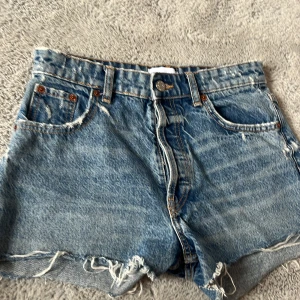 Blå jeansshorts från Zara - Snygga blå jeansshorts från Zara med fransiga kanter och knappgylf. Perfekta för en avslappnad stil. Klassisk femficksdesign och högmidjade för en trendig look.