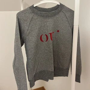 Grå tröja från Selected Femme - Säljer en stilren grå tröja från Selected Femme med röd text på framsidan. Tröjan har långa ärmar och en rund halsringning. Perfekt för en avslappnad look.