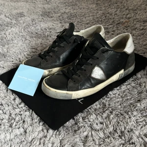 Svarta Philippe model skor - Snygga svarta skor med vita detaljer och snörning. Skorna har en stilren design med en kontrasterande vit häl och sula. Perfekta för en avslappnad stil.