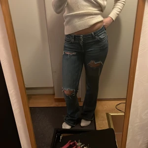 Blå bootcut jeans med slitningar - Snygga blå bootcut jeans med slitningar på knäna och låren. De har en lågmidjad passform och klassisk femficksdesign. Perfekta för en avslappnad stil.