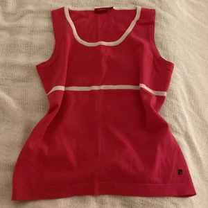 Rosa topp - Snygg rosa linne/topp från Redgreen med vita detaljer. Perfekt för varma dagar med sin ärmlösa design och bekväma passform. Enkelt att matcha med olika outfits.