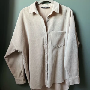 Beige damskjorta - Zara Basic (XS) - Säljer en stilren beige damskjorta från Zara Basic. Skjortan har en klassisk krage, knappar framtill och en bröstficka. Perfekt för en avslappnad look. Tillverkad i ett mjukt material som känns skönt mot huden (Polyester 88%, Nylon 9%, Elastan 3%) tillverkad i Marocko. Storlek XS (eu)