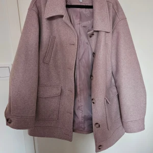 Ljusrosa kappa från NA-KD - Säljer en stilren ljuslila kappa från NA-KD. Jackan har en klassisk design med stora knappar och praktiska fickor framtill. Perfekt vårjacka 💖 sparsamt använd så i väldigt fint skick. Färgen är typ ljuslila?