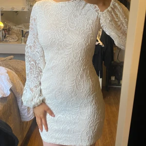 Studentklänning /Vit spetsklänning - Säljer en elegant vit spetsklänning med långärmade detaljer. Klänningen har en tight passform och är perfekt för speciella tillfällen. Den är kort och har ett vackert blommigt mönster som ger en romantisk känsla. Perfekt för vår och sommar!