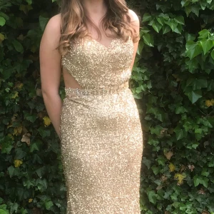 Glittrig guldklänning - Säljer en fantastisk glittrig guldklänning med öppen rygg och smala axelband. Klänningen har en figurnära passform och är dekorerad med paljetter som ger en glamorös look. Perfekt för speciella tillfällen! Jag är öppen för prisförslag:)