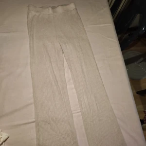 Beige ribbade byxor från Gina Tricot - Snygga beige ribbade mjukisbyxor från Gina Tricot i en mjuk och bekväm design. Perfekta för en avslappnad stil med en elastisk midja för extra komfort. Passar bra till både vardag och mysiga hemmakvällar.