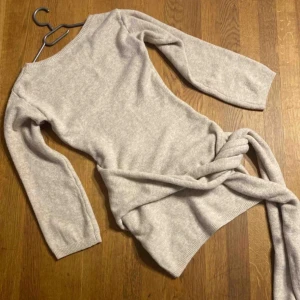 Beige stickad klänning - Säljer en superfin beige stickad klänning med lång ärm och knytband i midjan. Perfekt för en stilren look. Klänningen har en kort längd för mig som är 177.  Varm och mjuk