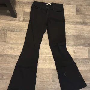 Svarta bootcut byxor från Lindex - Snygga svarta bootcut byxor från Lindex. Perfekta för en stilren look med en klassisk passform. Byxorna har en knapp och dragkedja framtill.