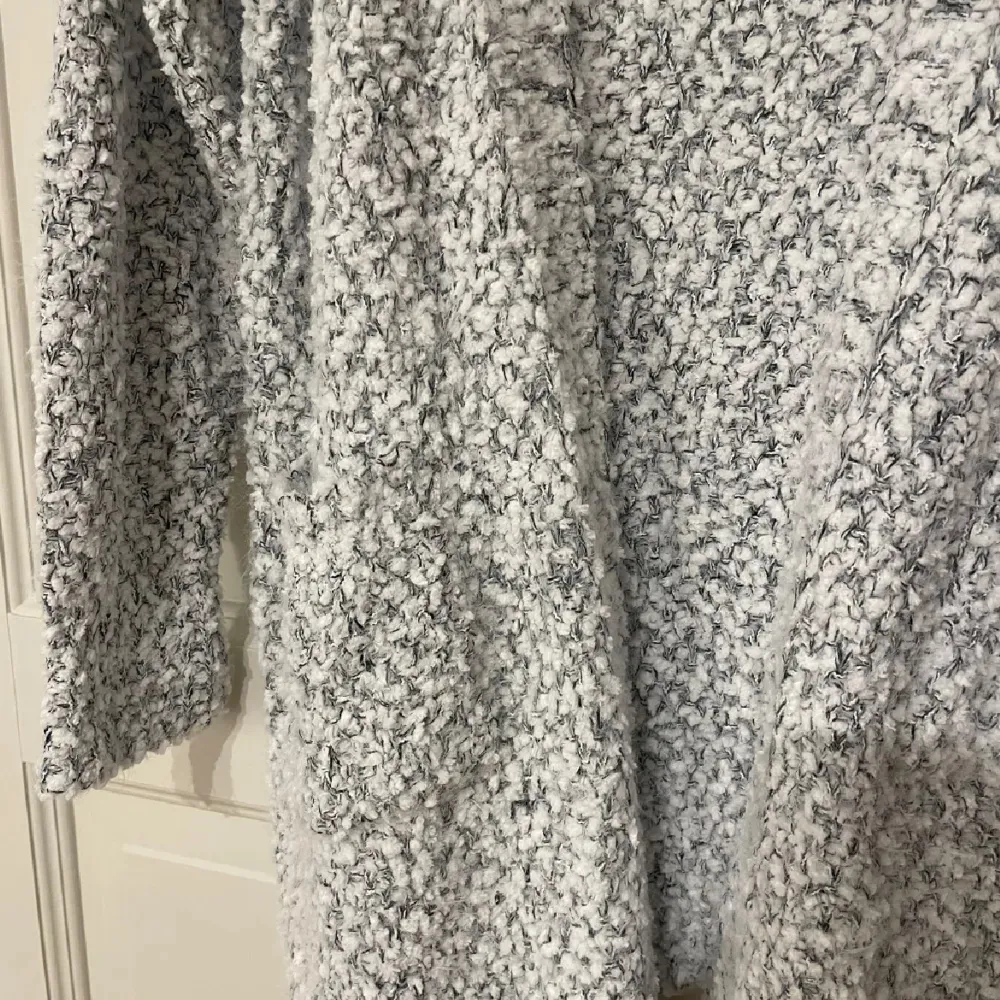 Mysig och fluffig grå stickad kofta med lång ärm och öppen design. Perfekt för kyliga dagar när du vill ha något bekvämt och stilrent. Koftan har en texturerad yta som ger en extra dimension till din outfit.. Neuletakit & Villapaidat.