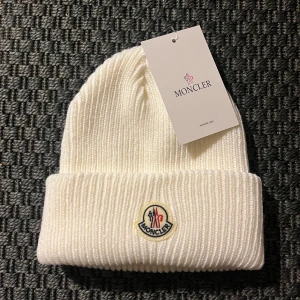 Vit Moncler Mössa - Snygg vit ribbad mössa från Moncler med broderad logotyp framtill. Perfekt för att hålla värmen under kyliga dagar. Stilren design som passar till det mesta. One Size.