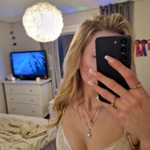 Smyckesset med halsband och örhängen - Elegant smyckesset med ett dubbelt halsband och matchande örhängen. Halsbandet har två hängen, ett med en rund sten och ett med en blomformad design, båda i glittrande silver. Örhängena är enkla och stilrena med runda stenar som matchar halsbandet. Ny pris 500kr, använt max 3 ggr.