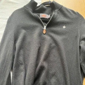 Svart tröja med dragkedja från Morris - Snygg svart tröja från Morris med dragkedja och liten broderad logga på bröstet. Perfekt för en stilren look. Tröjan har en hög krage och är tillverkad i ett mjukt material. I toppskick och använd en gång.