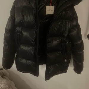 Moncler ecrin  - Snygg svart pufferjacka från Moncler med dragkedja och huva. Jackan har långa ärmar och två fickor med dragkedja framtill. Perfekt för kyliga dagar med sin quiltade design och stilrena, otroligt prisvärd att köpa nu innan nästa vinter look. Med storleken 4 