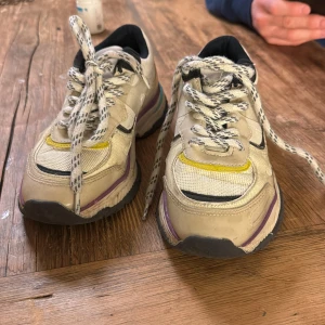Beige sneakers med färgglada detaljer - Snygga beige sneakers med svarta och gula detaljer samt lila och turkosa inslag på sulan. Skorna har snörning och en robust sula som ger bra stöd. 