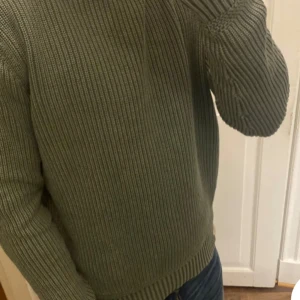 Grön stickad tröja från Morris Division - Säljer en stilren och unik grön stickad tröja från Morris Division. Tröjan har en ribbad struktur och långa ärmar. Perfekt för kyligare dagar och ger en klassisk look. Märkesdetalj på sidan ger en extra touch. Pris kan diskuteras 
