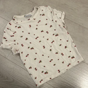 Vit t-shirt med blommor från Bershka - Säljer en söt vit t-shirt från Bershka med ett charmigt blommigt mönster. Den har korta ärmar och en rund halsringning. Perfekt för en avslappnad stil. 🍒