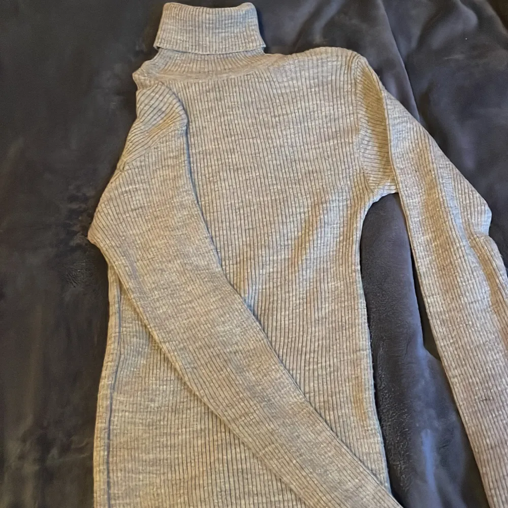 Snygg grå ribbad polotröja med långa ärmar. Perfekt för kyligare dagar och ger en stilren look. Passar bra till både jeans och kjol.. Neuletakit & Villapaidat.
