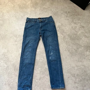Blå jeans från Lee - Snygga blå jeans från Lee med klassisk femficksdesign och knappgylf. Perfekta för en avslappnad stil. De har en rak passform och är tillverkade i slitstarkt denim.