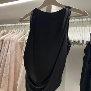 Svart satin topp från Zara - Elegant svart topp från Zara med en stilren design. Toppen har en knytning i ryggen som ger en fin detalj och en smickrande passform. Köpt från Zara, endast använd en gång🤎🤎