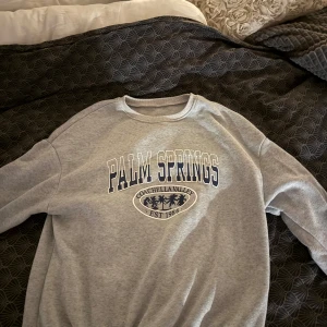 Grå sweatshirt med Palm Springs-tryck - Säljer en grå sweatshirt med tryck 'Palm Springs Coachella Valley Est. 1986' i blått och svart. Tröjan är från SHEIN storlek S och knappt använd 