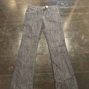 Blå lågmidgade bootcut jeans från Armani Jeans - Snygga blå jeansbyxor från Armani Jeans med klassisk femficksdesign. Byxorna har en bootcut-stil och är perfekta för en avslappnad look. De är tillverkade i ett slitstarkt denimtyg och har en knapp- och dragkedjestängning. Byxorna har glitter i tygen som syns när solen ligger på. Perfekta till vardags om man vill spicya upp looken. 