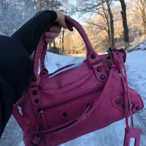Rosa handväska från Balenciaga - Belenciaga city bag som inte tillverkas eller säljs längre. Snygg färg som sticker ut. Perfekt storlek 34x19 cm . Orginalpris är 18.000 men säljer för 5000. Lite slitningar på väskan men fortfarande bra kvalite och skick. Äkthetsbevis och serie nummer finns, vid intresse hör av dig så kan jag skicka privat! 💞💞