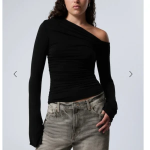 Svart oneshoulder topp - Snygg svart oneshoulder topp med lång ärm och rynkade detaljer. Perfekt för en stilren och modern look.