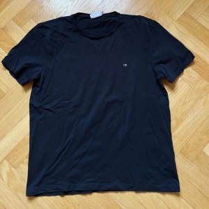 Svart t-shirt från Calvin Klein - Säljer en stilren svart t-shirt från Calvin Klein i storlek L. T-shirten har en liten CK-logga på bröstet och är tillverkad i ett mjukt material. Perfekt för en enkel och klassisk look.