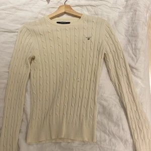 Vit stickad tröja från GANT - Säljer en  creme vit stickad tröja från GANT med kabelstickat mönster. Tröjan har långa ärmar och en rund halsringning. Som man ser på fjärde bilden har en sömn gått av men inget som märks och går säkert att fixa enkelt. Förutom sömmen är tröjan i nyskick därav priset. Skriv ett meddelande för funderingar eller prisförslag 💕