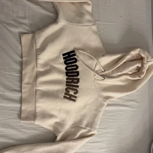 Vit hoodie från Hoodrich - Säljer en snygg vit hoodie från Hoodrich med stor text på bröstet. Den har en klassisk huva med dragsko och ribbade muddar vid ärmslut och nederkant. Perfekt för en avslappnad stil, använd 3 gng.