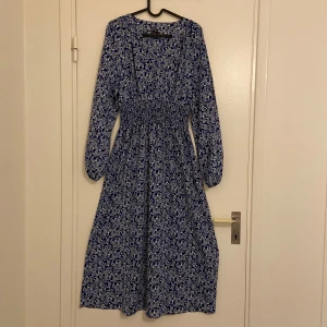 Blå  klänning från Shein - Säljer en blå långklänning från Shein med ett vitt paisleymönster. Klänningen har långa ärmar och en smockad midja som ger en fin passform. Perfekt för en stilren look!