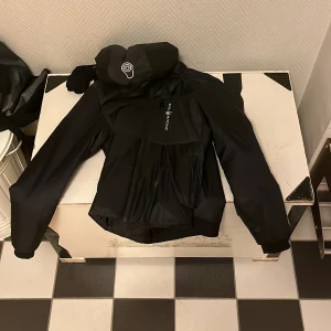 Svart jacka från sail racing - Säljer en svart jacka från Dainese med långärmad design och dragkedja. Perfekt för motorcykelentusiaster som vill ha stil och säkerhet. Jackan har en modern look och är tillverkad i slitstarkt material.,strl 150