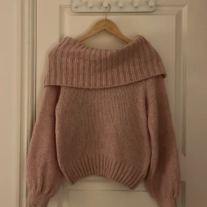 Rosa stickad offshoulder tröja - Mysig rosa stickad tröja med offshoulder-design och långa ärmar. Perfekt för kyliga dagar med sin ribbade krage och muddar. Liten i storlek.