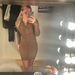 Brun tight klänning - Snygg brun tight klänning med långa ärmar och knappar framtill. Perfekt för en stilren look.